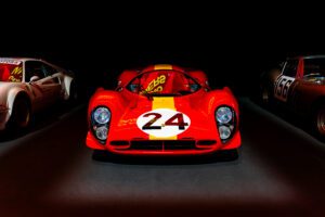 Classic red Ferrari race car displayed under spotlight in an exhibition